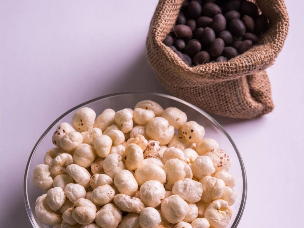 Bowl of popped fox nuts next to unpopped seeds